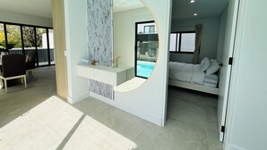 Een moderne hotelkamer met een groot raam, een bed, een zithoek met een tafel en stoelen, en uitzicht op een zwembad.