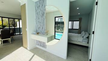 A modern hotel room with a large window, a bed, a seating area with a table and chairs, and a view of a swimming pool.