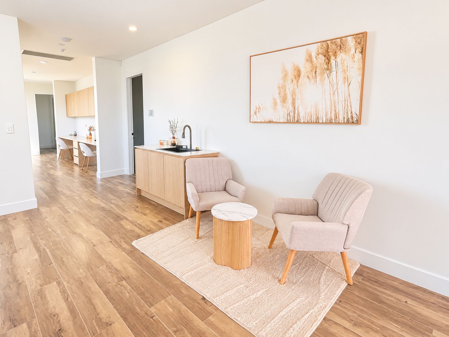 A modern living room with a wooden floor, two armchairs, a round coffee table, and a kitchen area with a sink and cabinets.