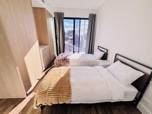 A hotel room with two beds, a wardrobe, and a large window with curtains.