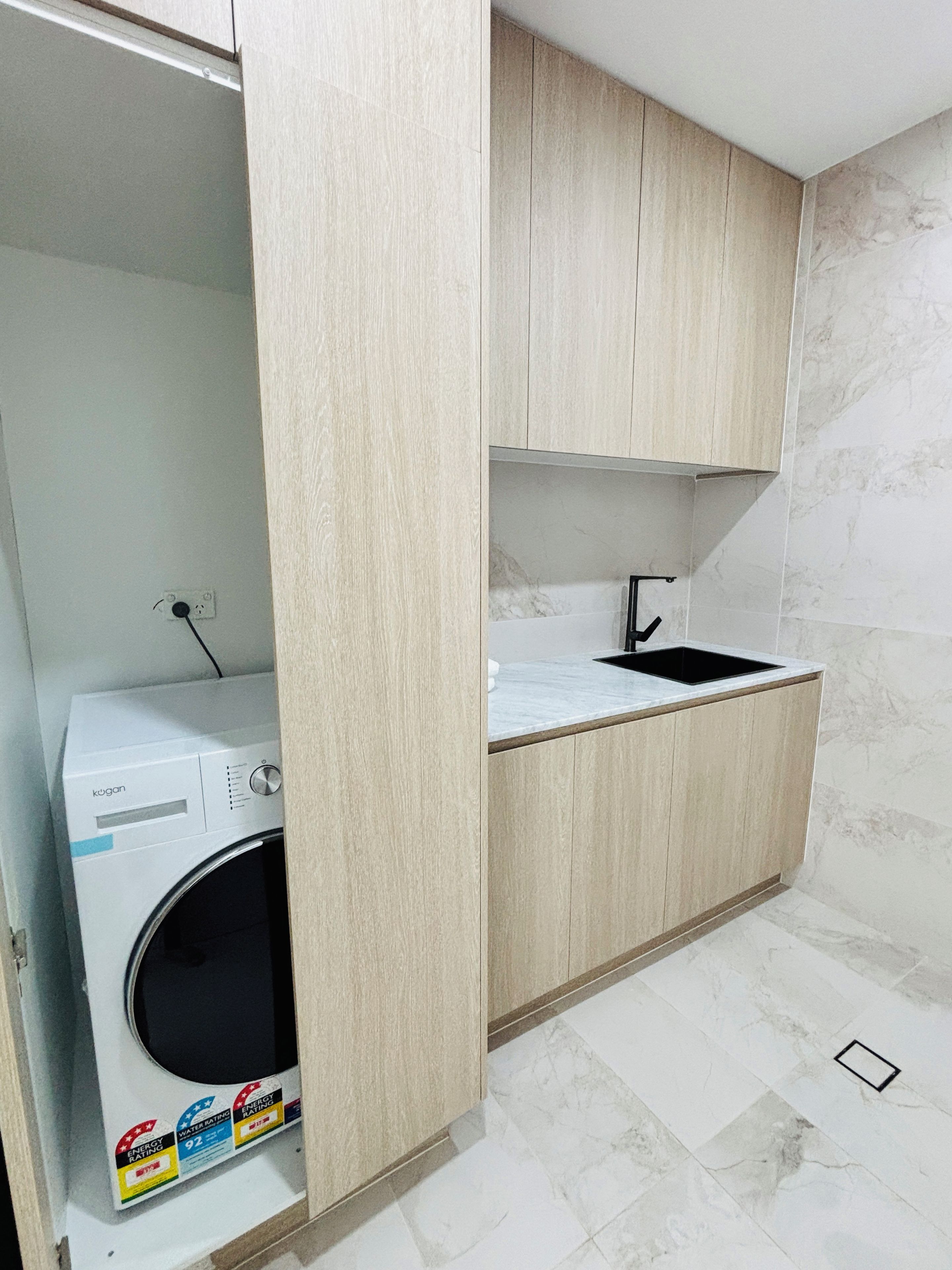 Une cuisine compacte dotée d’un lave-linge encastré, d’un évier et d’un sol carrelé en marbre.
