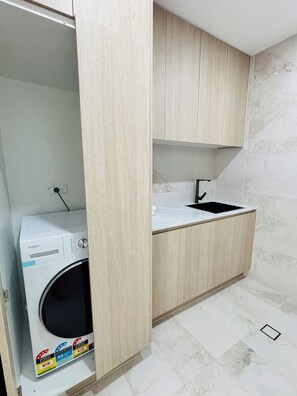 A compact kitchen with a built-in washing machine, a sink, and a marble-tiled floor.