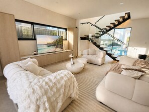 A modern living room with a sofa, coffee table, and a large TV screen. - Spacious 5-Bedroom Resort-Style Sydney Family Home with Private Swimming Pool (Bexley)