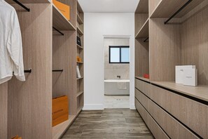 A narrow walk-through closet with wooden shelves and hanging space, featuring luxury brand labels.