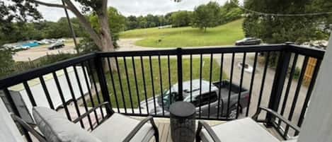 A deck with two chairs and a small table, overlooking a grassy area with parked cars.