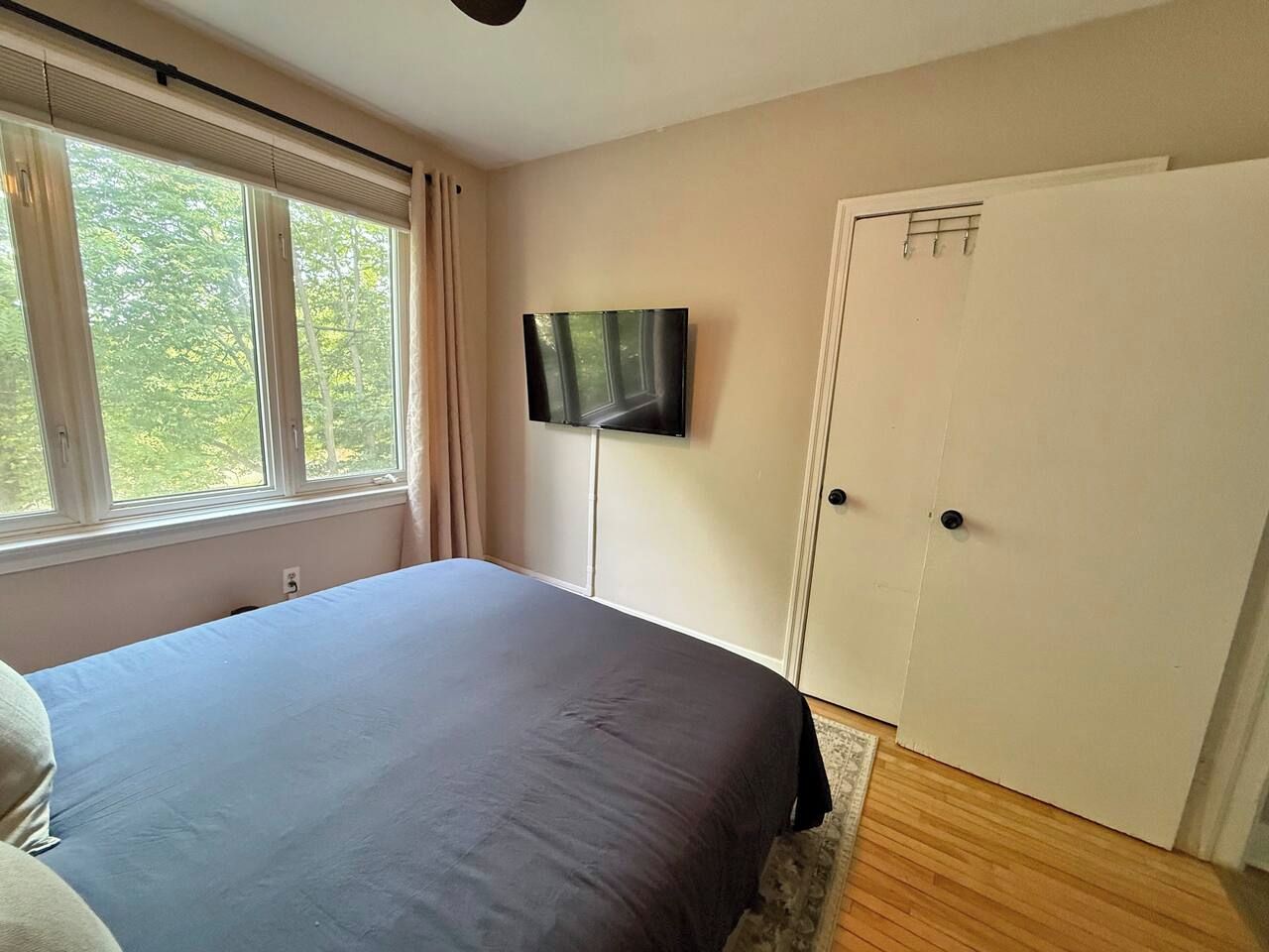 A bedroom with a bed, a television on the wall, a window with curtains, and a door.