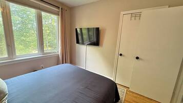 A bedroom with a bed, a television on the wall, a window with curtains, and a door.