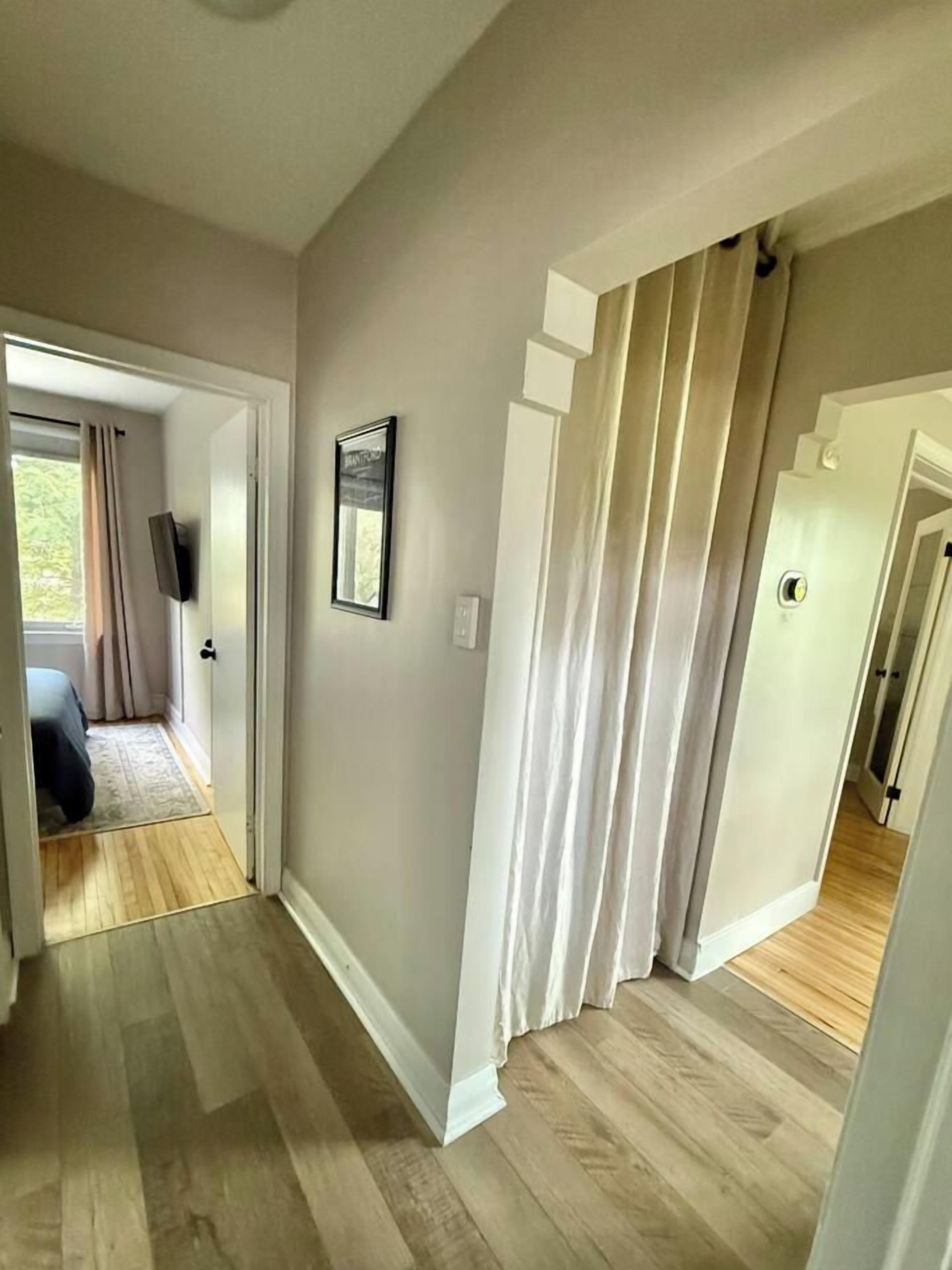 A hallway with a wooden floor, a door leading to a bedroom, and a staircase.