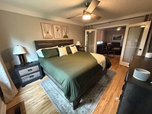 Quarto com cama, mesas de cabeceira, escrivaninha e ventilador de teto.