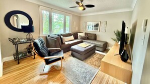 A modern living room with a sofa set, a coffee table, a TV stand, and a ceiling fan. - Spacious 2BR Retreat w/Balcony & Gazebo (Brantford)