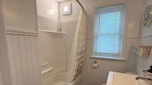 A bathroom with a bathtub, a toilet, a sink, and a window with blinds. - Spacious 2BR Retreat w/Balcony & Gazebo (Brantford)