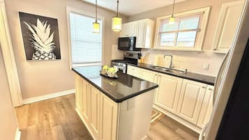 A kitchen with a central island, white cabinets, a microwave, and pendant lights.