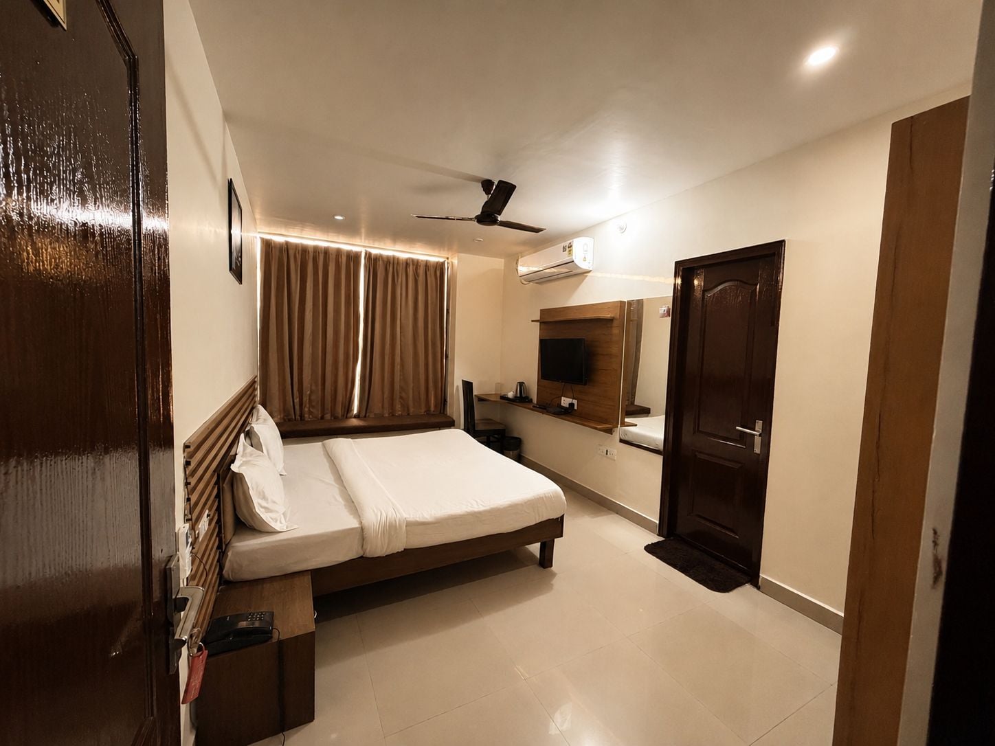 Una habitación de hotel con cama, ventilador de techo, televisor y espejo.
