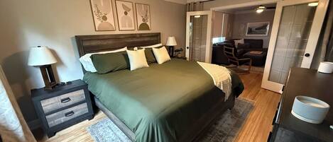 Une chambre à coucher comprenant un lit, des tables de chevet, une commode, un ventilateur de plafond et une porte donnant sur une autre pièce.