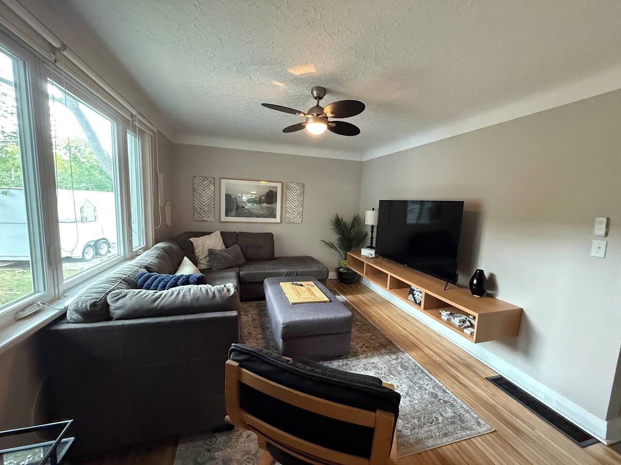 Een moderne woonkamer met een bank, een poef en een televisie op een houten standaard.