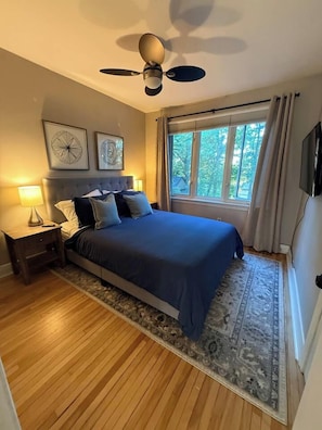 Quarto com cama, ventoinha no teto, janela com cortinas e tapete.