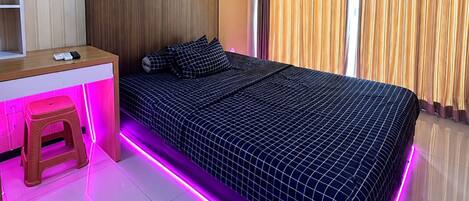 A bedroom with a bed, a desk, and a stool.