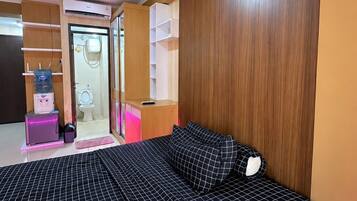 A bedroom with a bed, a wooden headboard, a bathroom with a toilet and sink, and a water dispenser.