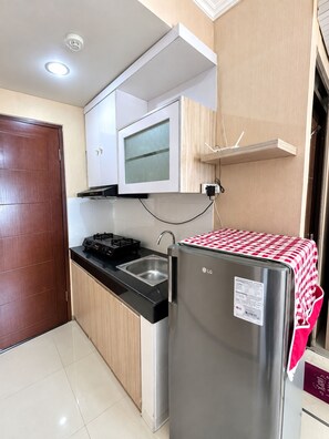 Cocina compacta con refrigerador de acero inoxidable, estufa a gas, pileta y mueble de madera con ventanal de vidrio esmerilado.