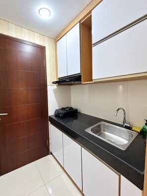 A kitchen with a black countertop, stainless steel sink, and a wooden door. - Gateaway Pasteur by Sewa Apart Bandung (Kota Bandung)