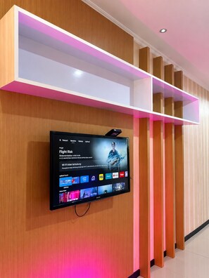Un televisor de pantalla plana montado en una pared de madera con un estante iluminado en rosa arriba.