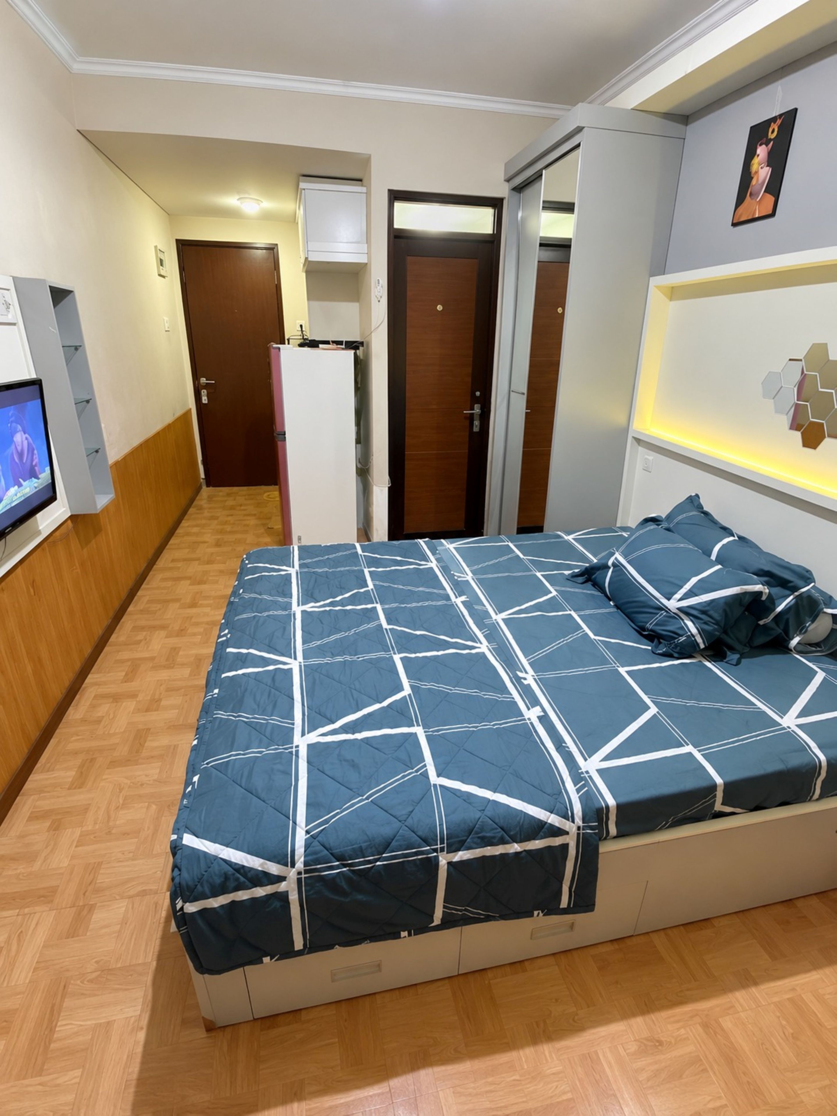 Un dormitorio con una cama, televisión, una puerta y una lámpara fijada a la pared.
