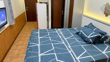 Un dormitorio con una cama, televisión, una puerta y una lámpara fijada a la pared.