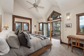 Een slaapkamer met een bed, een plafondventilator, een bureau en uitzicht op de omgeving.