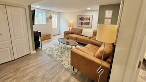 A living room with a sofa, coffee table, and a lamp. - Modern 2BR Retreat w/ Heated Floors & Gazebo (Brantford)