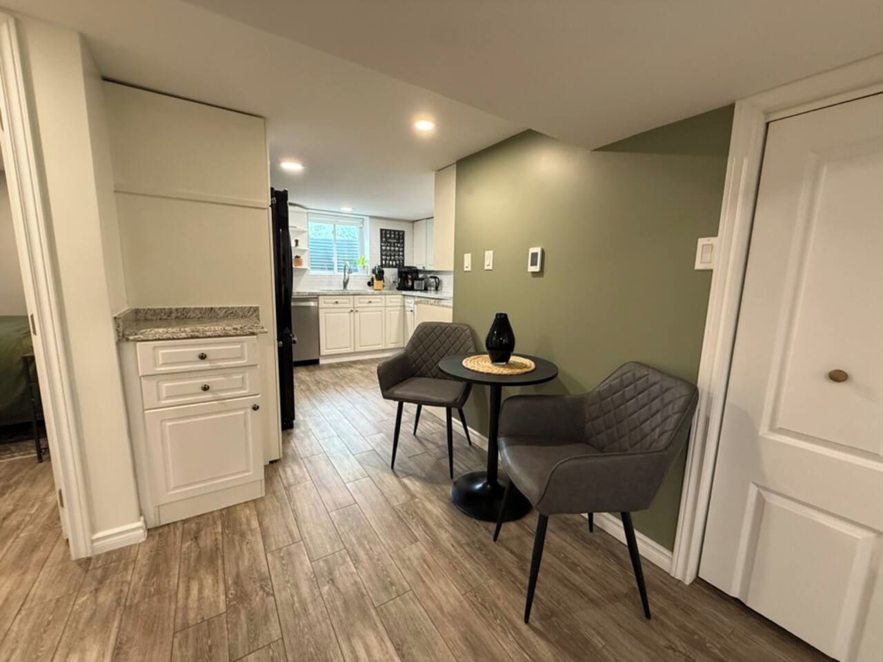 A compact kitchen with white cabinetry, a dining area with two chairs and a small table, and a green accent wall.
