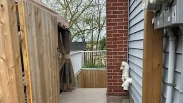 A wooden fence, a concrete pathway, and a brick wall with a window and electrical boxes.