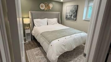 Un dormitorio con una cama, una mesita de noche, una lámpara, una obra de arte colgada en la pared y una alfombra estampada.