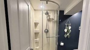 A bathroom with a glass-enclosed shower, a toilet, and a dark wall. - Modern 2BR Retreat w/ Heated Floors & Gazebo (Brantford)