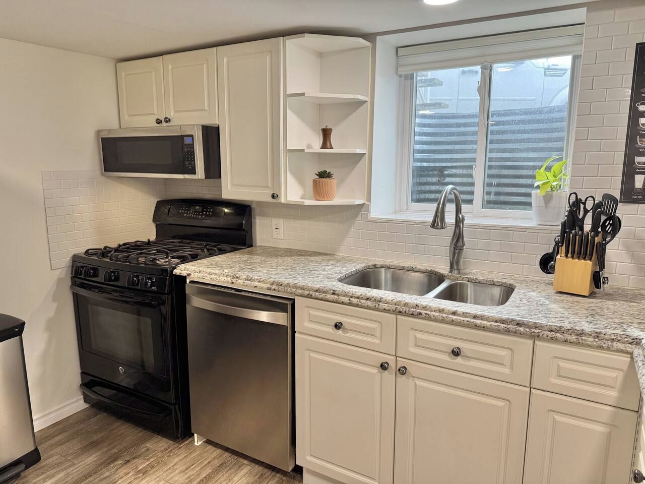 A kitchen with white cabinets, a stainless steel sink, a microwave, a stove, and a dishwasher.