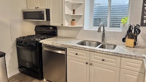 A kitchen with white cabinets, a stainless steel sink, a microwave, a stove, and a dishwasher. - Modern 2BR Retreat w/ Heated Floors & Gazebo (Brantford)