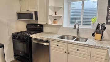 A kitchen with white cabinets, a stainless steel sink, a microwave, a stove, and a dishwasher.