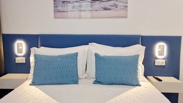 Habitación de hotel con una cama, dos mesitas de noche, una lámpara de pared y una imagen del océano.