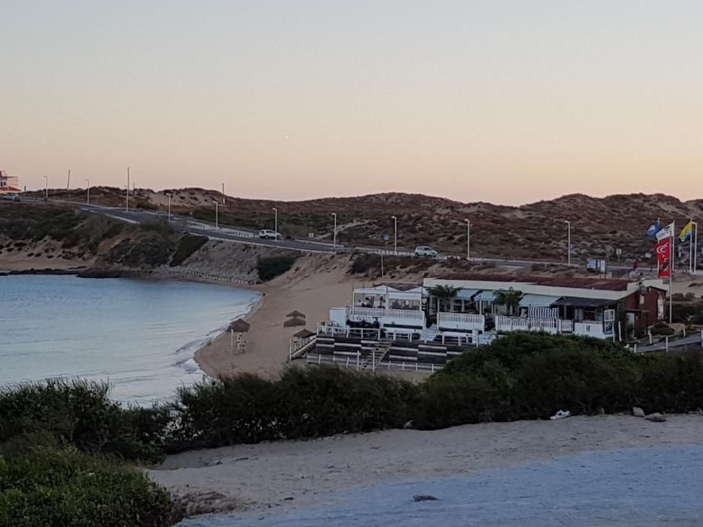 A coastal hotel with a beach view, a road, and a hilly landscape.