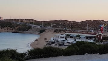 A coastal hotel with a beach view, a road, and a hilly landscape.
