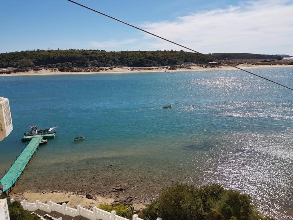 A coastal view with a pier extending into calm waters, boats docked, and a beach in the background.