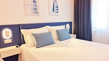 A hotel room with a bed, bedside tables, a nightstand, a chair, and artwork on the wall.