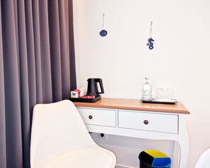 A hotel room with a wooden desk, a white chair, a coffee maker, a bottle of water, and a small shelf with decorative items. - Golfinho Azul (Odemira)