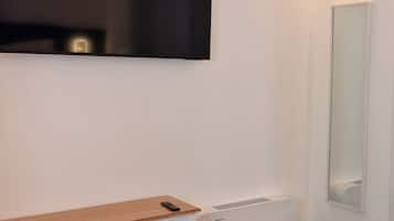 A room with a white desk, a mirror, and a wall-mounted television.