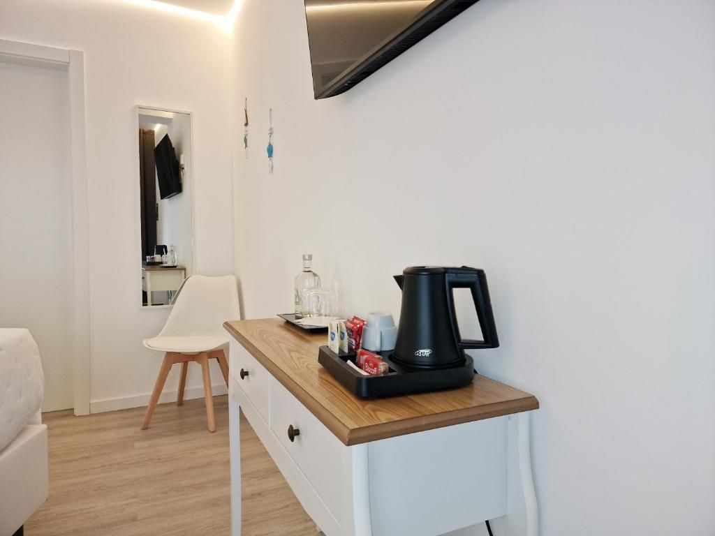 Una pequeña cocina americana con cafetera, hervidor de agua y una bandeja con tazas y un vaso. Hay una silla blanca y un sofá blanco en la habitación.