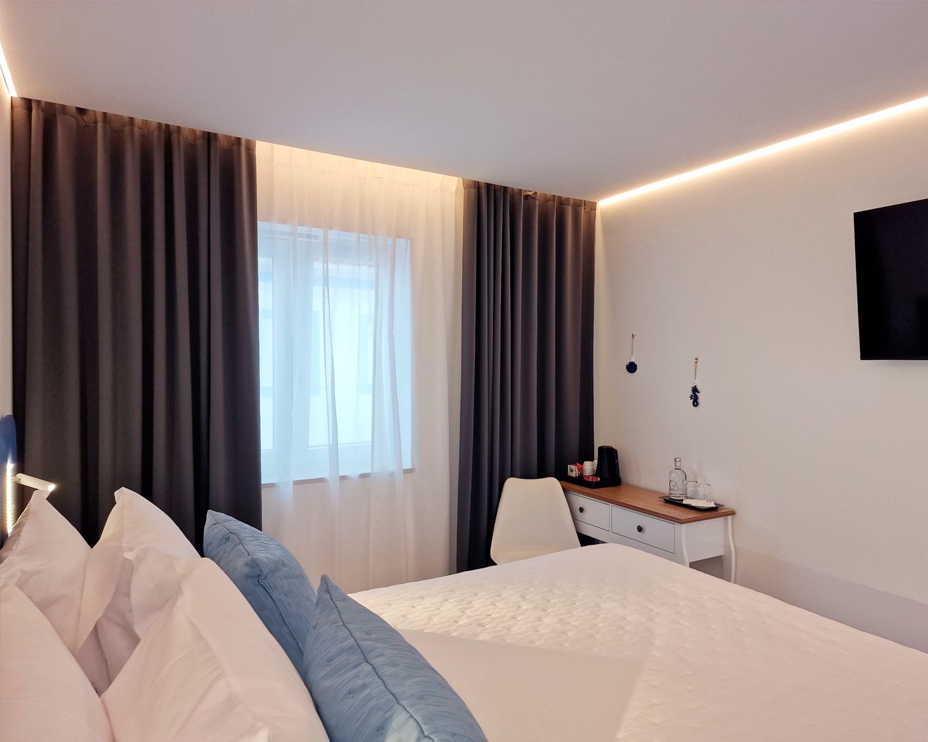 A hotel room with a bed, a desk, a chair, a TV, and curtains.