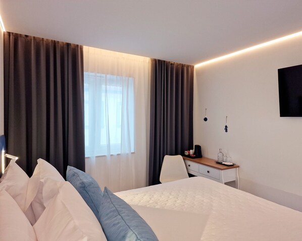 A hotel room with a bed, a desk, a chair, a TV, and curtains. - Golfinho Azul (Odemira)