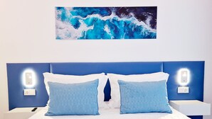 Una cama con colchón blanco, dos almohadas azules y cabecera azul. Hay dos mesitas de noche con interruptores iluminados.