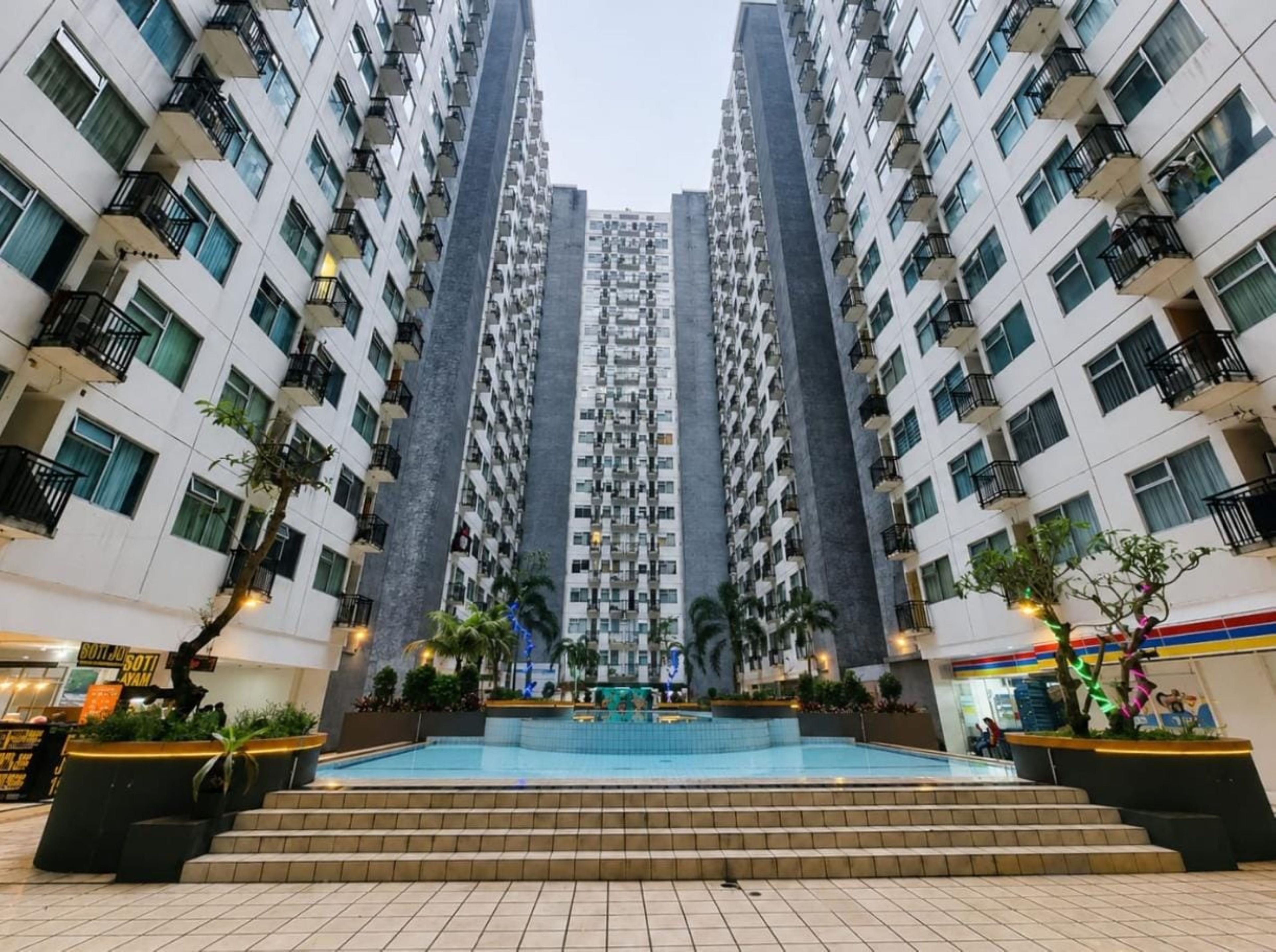 A high-rise residential building with multiple balconies, a central courtyard with a pool, and surrounding greenery.