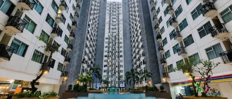 Un edificio residencial alto con varios balcones, un patio central con piscina y áreas verdes circundantes.
