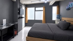 Moderni hotellihuone, jossa on sänky, televisio, työpöytä ja ikkuna, jossa on verhot.